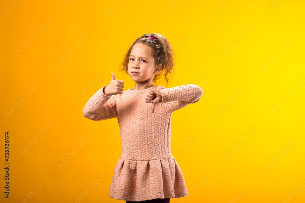 Child girl showing thumb up and thumb down gesture. Positive and negative emotions concept