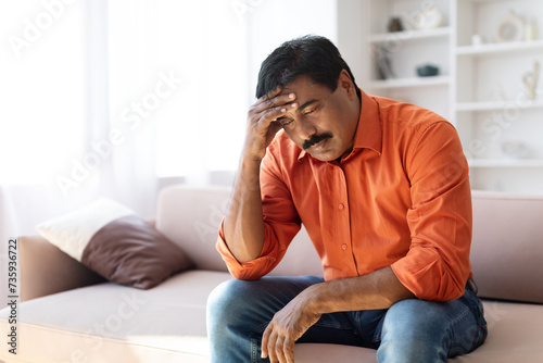 Upset frustrated indian man touching his head, living room interior