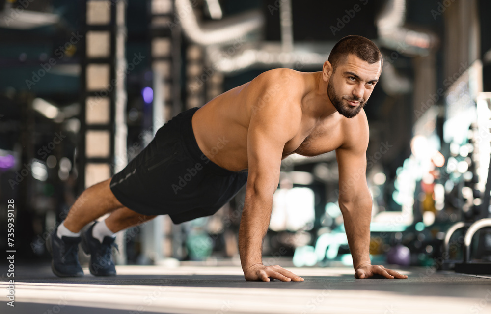 Focused man doing mid-push-up exercise while training at gym Focused man doing mid-push-up exercise while training at gym