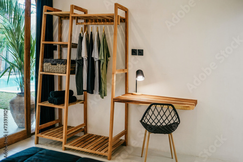 Wooden hangers with clothes on rack and small table with chair in the room © Roman