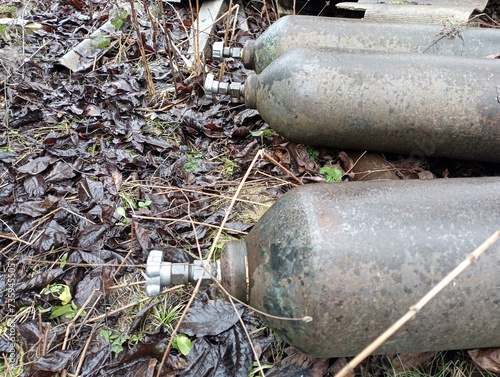 Three large metal oxygen cylinders lie outside on the ground. Storage of oxygen cylinders in violation of operational requirements.