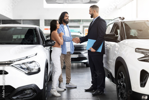 Car advisor stands discussing financing options with interested indian couple photo