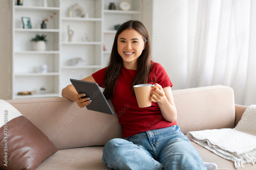 Relaxed asian woman holding cup of coffee and using digital tablet Relaxed asian woman holding cup of coffee and using digital tablet