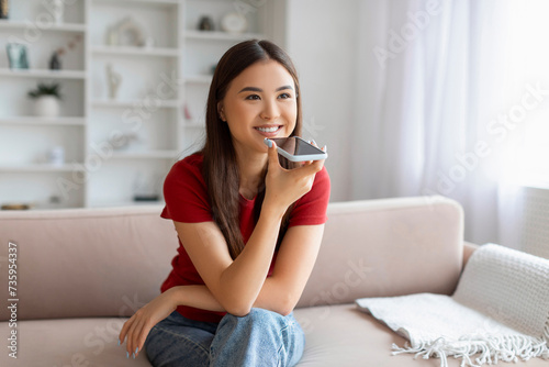 Portrait Of Smiling Young Asian Woman Recording Voice Message On Smartphone