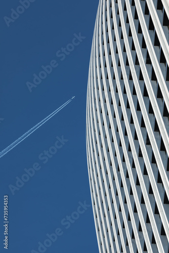 Obraz na płótnie Detail of a skyscraper against a clear blue sky with an airplane trace. w salonie