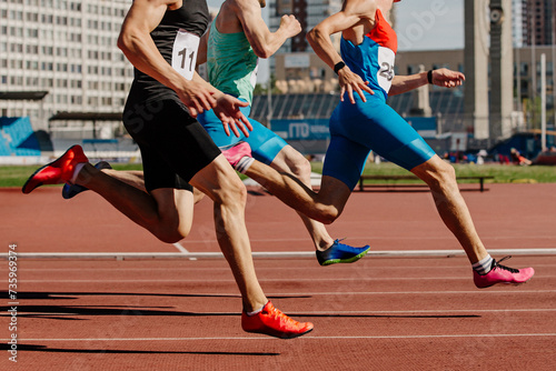 three male athletes sprinting on red track, muscles taut, competing fiercely. Brightly colored shoes emphasize motion
