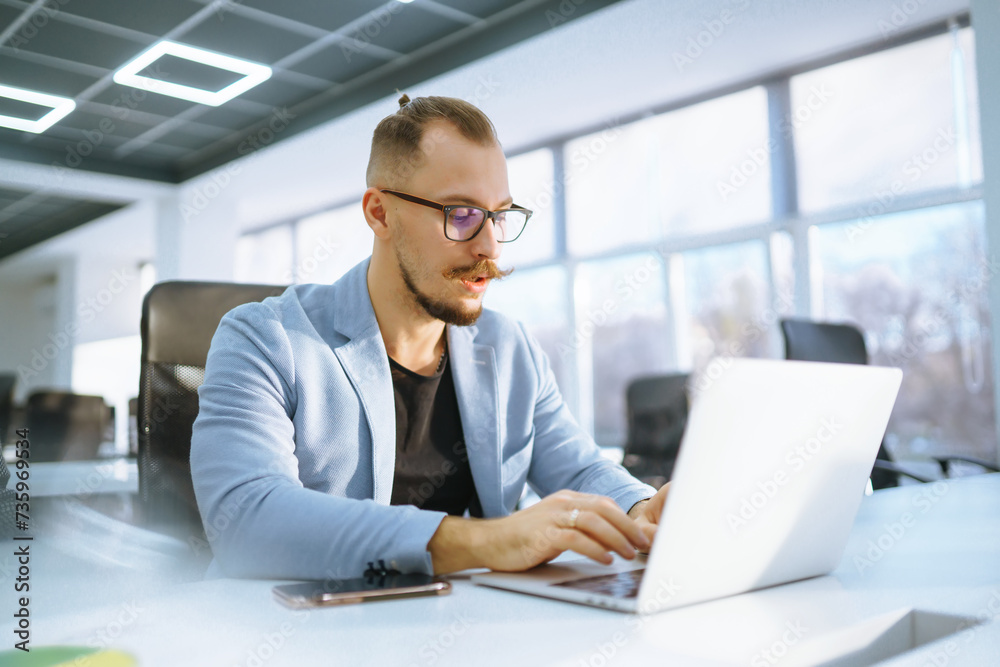 Young man wearing glasses working with laptop while sitting at his working place. Business, technology, study. Young man wearing glasses working with laptop while sitting at his working place. Business, technology, study.