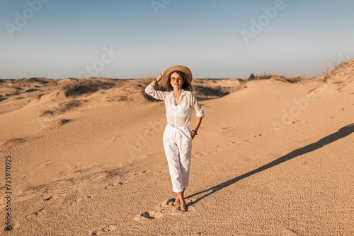 stylish beautiful carefree happy woman walking in desert sand dressed in white outfit