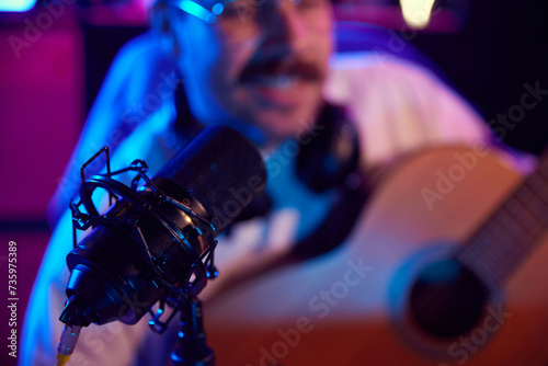 Studio microphone against blurred background with male artist  blogger  playing guitar and recording music in neon light. Concept of youth people with social media and smart working  lifestyle.