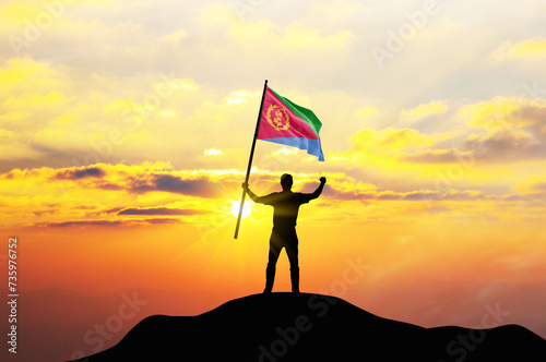 Eritrea flag being waved by a man celebrating success at the top of a mountain against sunset or sunrise. Eritrea flag for Independence Day. photo