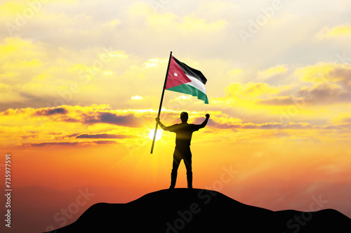 Jordan flag being waved by a man celebrating success at the top of a mountain against sunset or sunrise. Jordan flag for Independence Day.