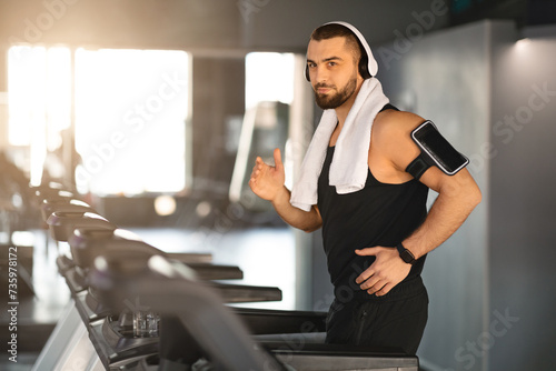 Muscular Male Athlete Wearing Wireless Headphones Running On Treadmill At Gym