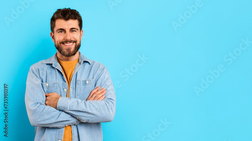 Happy millennial guy confidently stands with arms crossed in studio photo