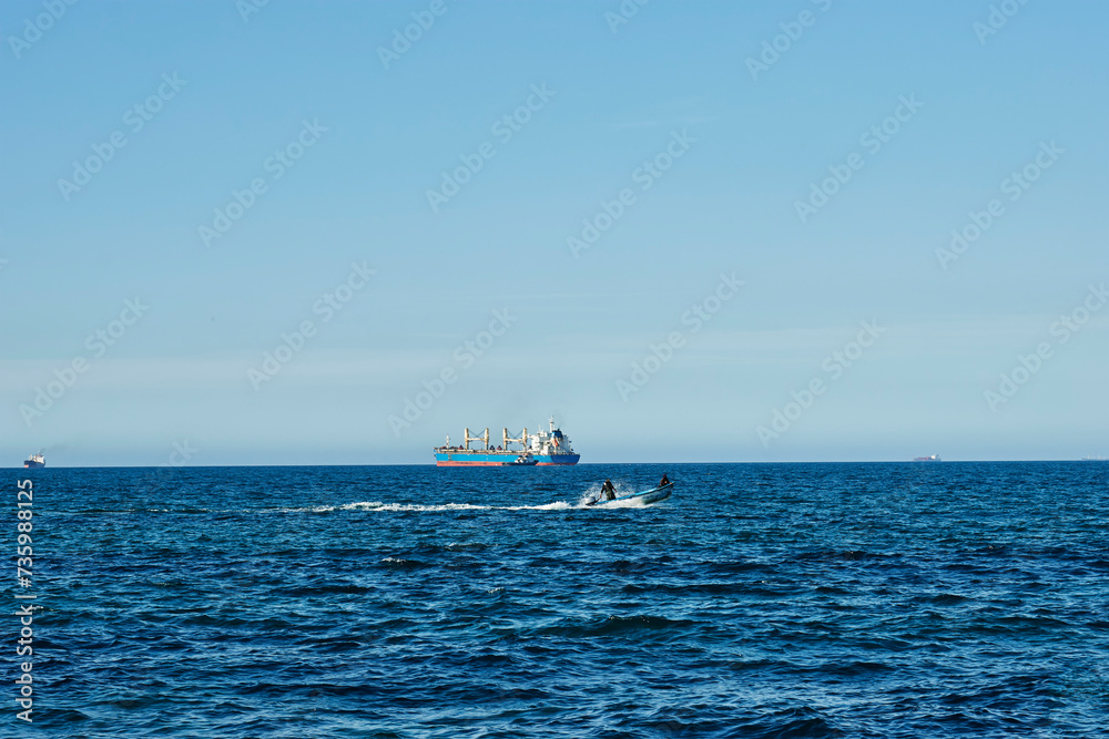 Mascara, Sig - Algeria - February 13 2024: a view of large container cargo and fishing boat on tranquil, sunny blue ocean
