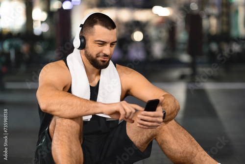 Handsome Young Athlete Man Relaxing With Smartphone After Training In Gym