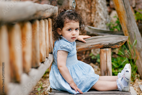 Obraz na płótnie Capturing innocence. Curly-haired two-year-old girl sitting on a wooden bench in the park and looking at camera w salonie