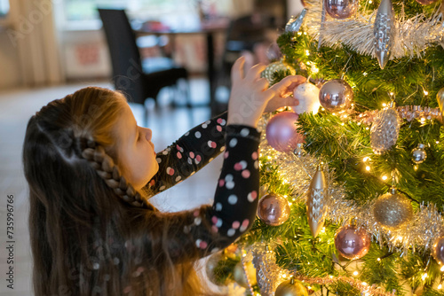 Single mum helping her daughters place ornaments on their tree. A beautiful bonding moment with twinkle lights and baubles. photo