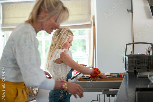 Young girl reaching for a sharp knife, helped by her mother to be clean and safe photo