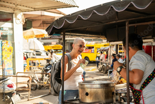 Mid aged woman solo traveller stops to buy street food from a vendor in Chiang Mai. Thailand photo
