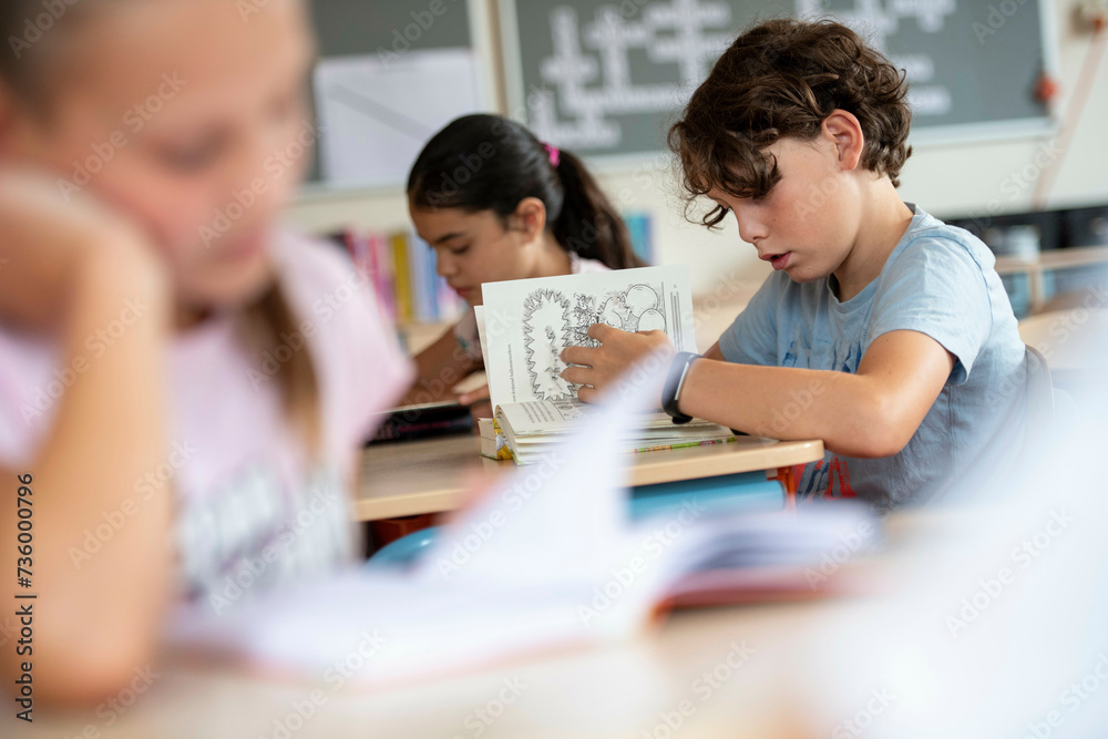 Young boy studying her text book in class Young boy studying her text book in class