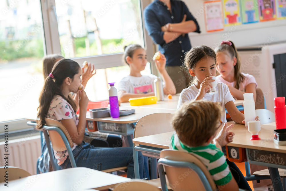 Male teacher sitting with his students in class at break time while they have lunch Male teacher sitting with his students in class at break time while they have lunch