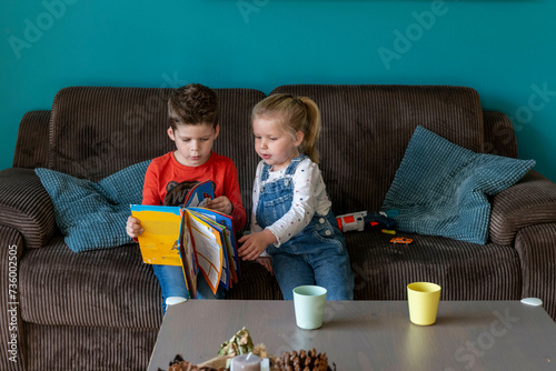 Brother and sister bonding sitting together on the sofa reading a story book