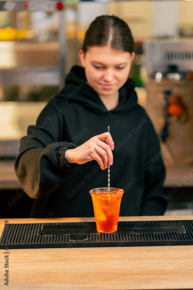 close-up of a young girl at the bar counter in the process of adding orange slices to cocktail with tweezers