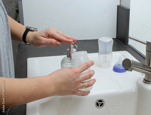 Close up of mothers hands cleaning a baby milk bottle with a brush  home kitchen sink