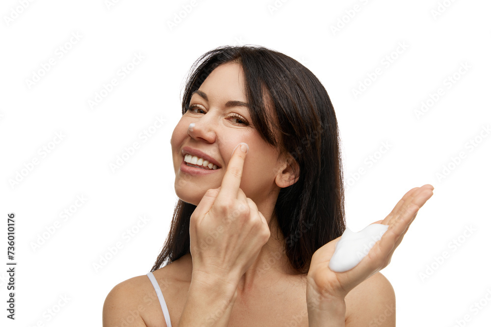 Portrait of smiling middle-aged woman applying foamy facial dermatology cosmetic product against white studio background. Concept of beauty and self care, wellness, skincare, hygiene procedures. Portrait of smiling middle-aged woman applying foamy facial dermatology cosmetic product against white studio background. Concept of beauty and self care, wellness, skincare, hygiene procedures.