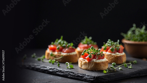 Bruschetta with cream cheese and a slice of tomato decorated with microgreens on a black slate table, space for text, banner