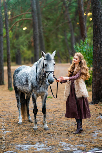 Portrait of beautiful blonde curl girl in medieval dress and fur vest on  nature with horse. Young worker in rural scene in forest.Warm colorful art work.  © Ольга Бойко