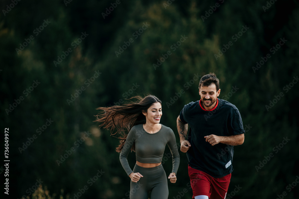 Naklejka premium Fit couple jogging amidst a scenic mountain landscape, dressed in sporty attire