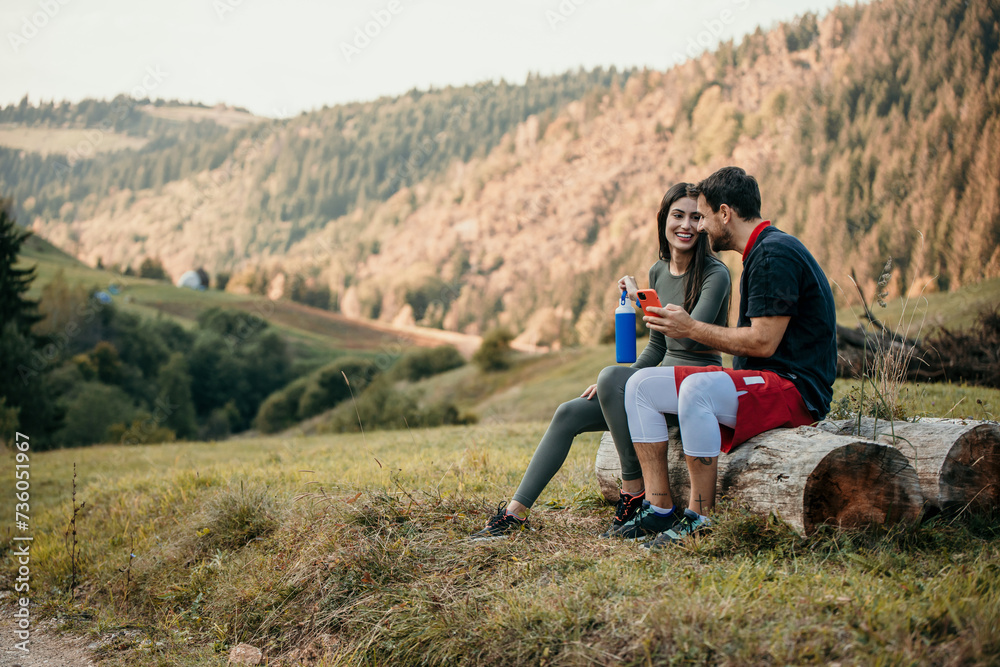 Diverse man and woman in fitness gear enjoying a water break while staying connected with their smart devices