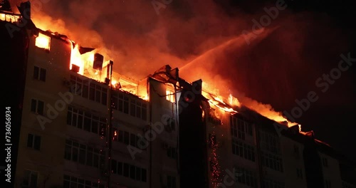 Fire blazing in apartment building. Burning house is engulfed in flames at night. Firefighters extinguish with water