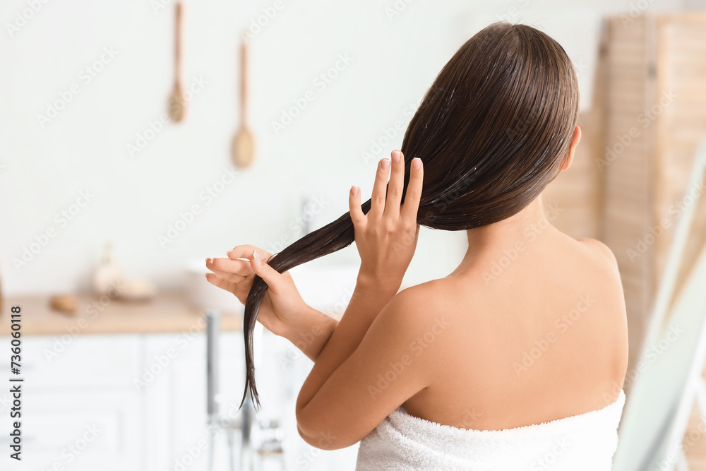 Beautiful young woman applying coconut oil onto her hair in bathroom, back view Beautiful young woman applying coconut oil onto her hair in bathroom, back view