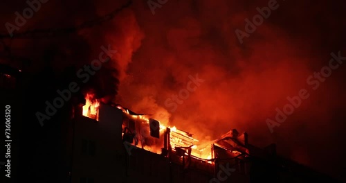 Huge fire blazing in apartment building. Burning house is engulfed in flames at night during the disastrous