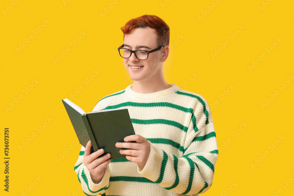 ?Young man in eyeglasses reading book on yellow background ?Young man in eyeglasses reading book on yellow background