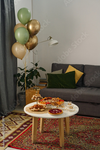 Traditional homemade snacks prepared for celebrating Eid al-Fitr standing on small round table against comfortable couch with cushions photo