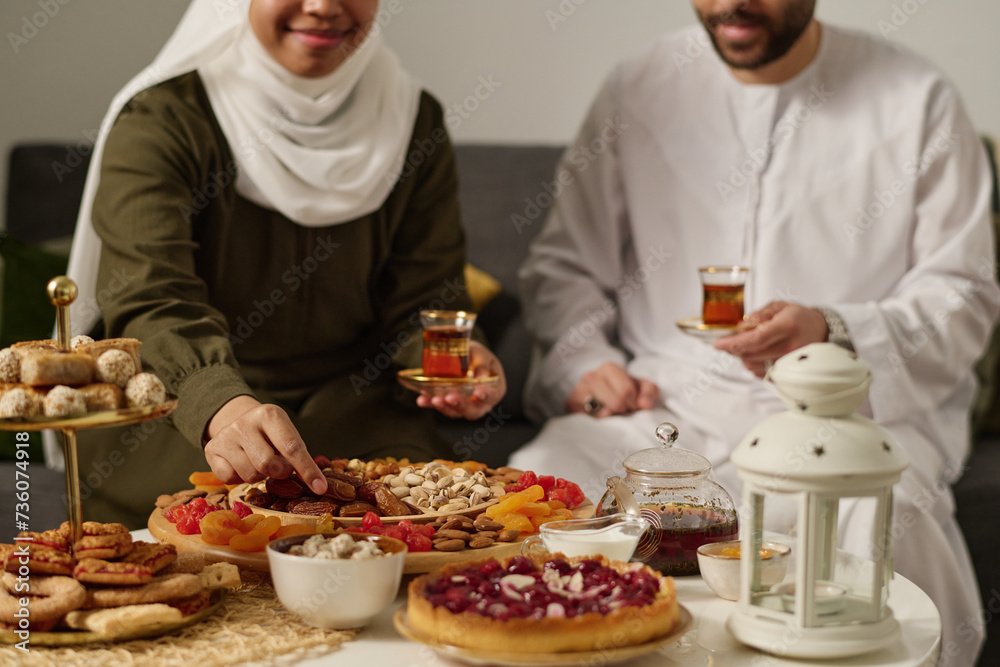 Young traditional Muslim couple in national clothes sitting in front of served table and having tea with dried and candied fruits Young traditional Muslim couple in national clothes sitting in front of served table and having tea with dried and candied fruits