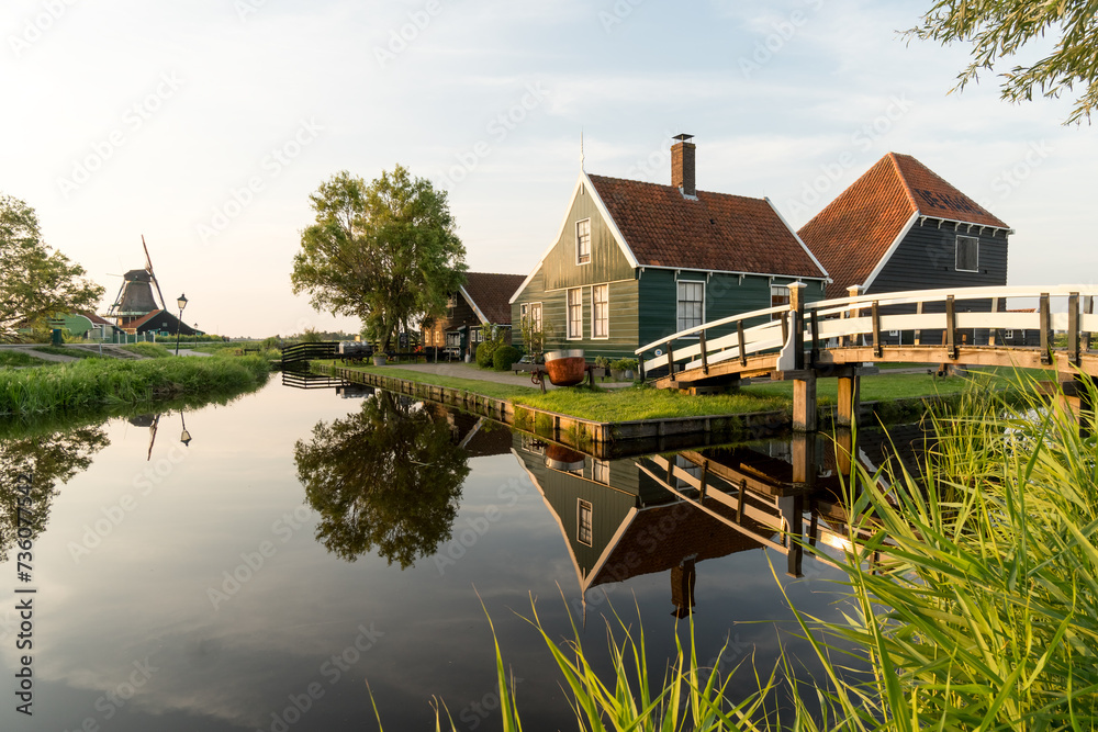 Obraz premium Beautiful village of Zaanse Schans in Netherlands at sunset with the wooden houses and the bridge reflected on the canal in a sunny day. Netherlands.