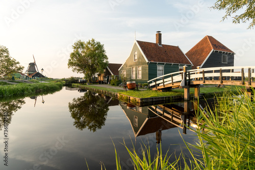 Beautiful village of Zaanse Schans in Netherlands at sunset with the wooden houses and the bridge reflected on the canal in a sunny day. Netherlands.