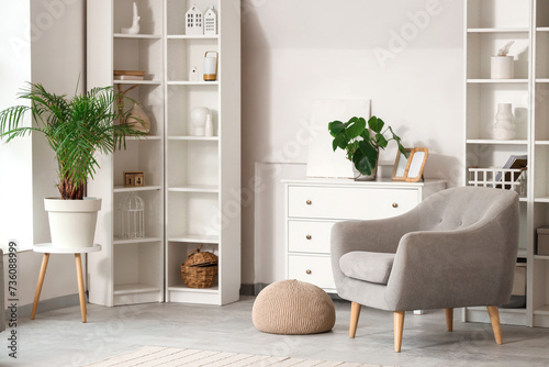 Interior of modern living room with grey armchair, drawers and shelf units