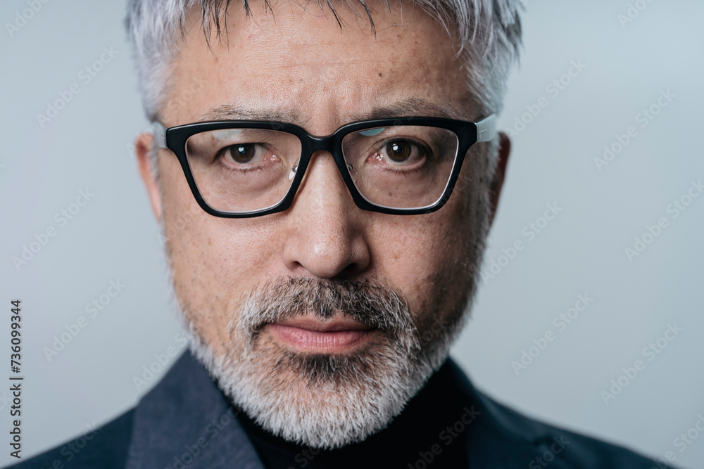ジャケットを着てメガネをかけている白髪まじりのミドル男性の顔のアップ ジャケットを着てメガネをかけている白髪まじりのミドル男性の顔のアップ