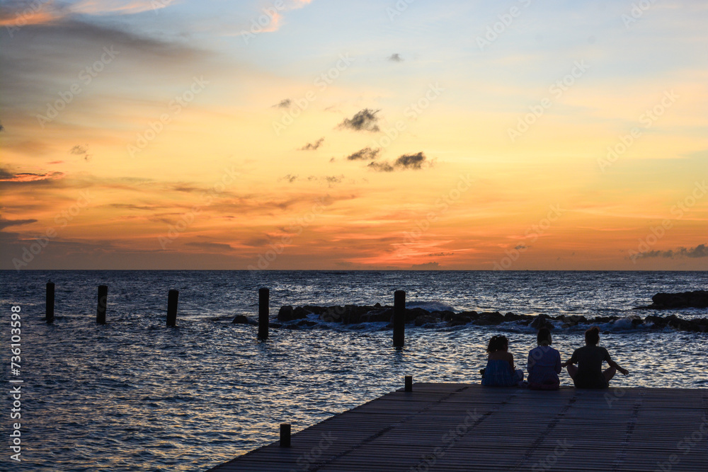 Obraz premium People sitting on the jetty during sun setting in Caribbean sea.