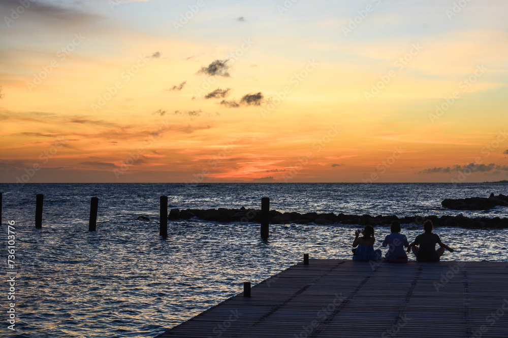People sitting on the jetty during sun setting in Caribbean sea.