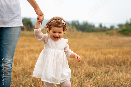 Mother little child holding hands walking in a grass field.Stock photo .