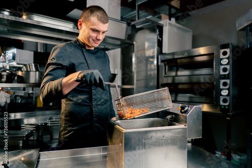 the chef in the kitchen in a black jacket takes out baht from the deep fryer photo