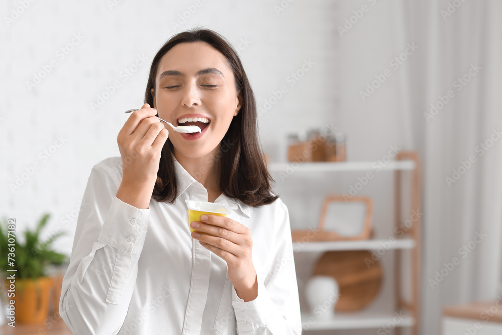 Happy young woman eating tasty yoghurt in kitchen Happy young woman eating tasty yoghurt in kitchen