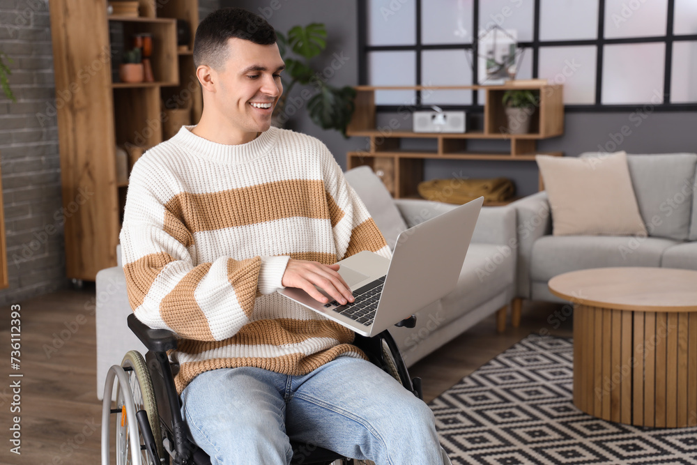 Happy young man in wheelchair using laptop at home