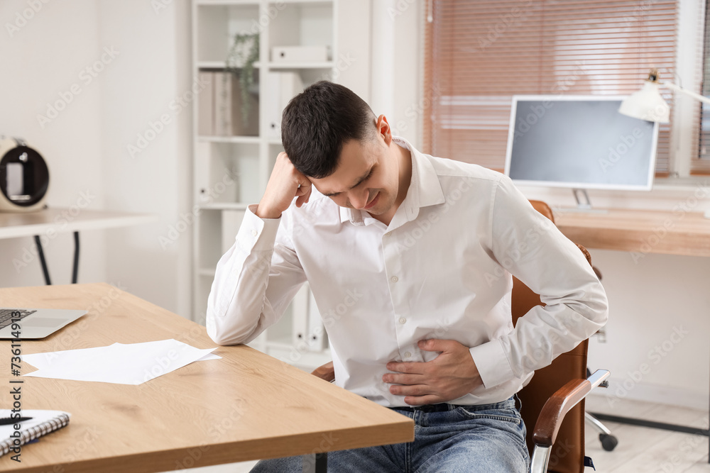Young businessman suffering from bellyache in office Young businessman suffering from bellyache in office